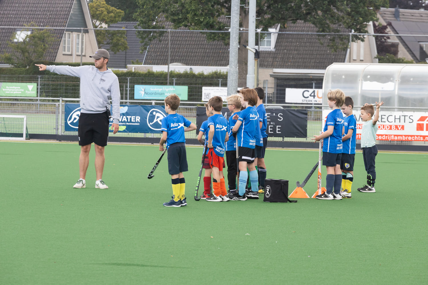 Kinderen tijdens ProHockey zomerkamp bij hockeyclub Prinsenbeek krijgen instructies op het veld van hun coach.