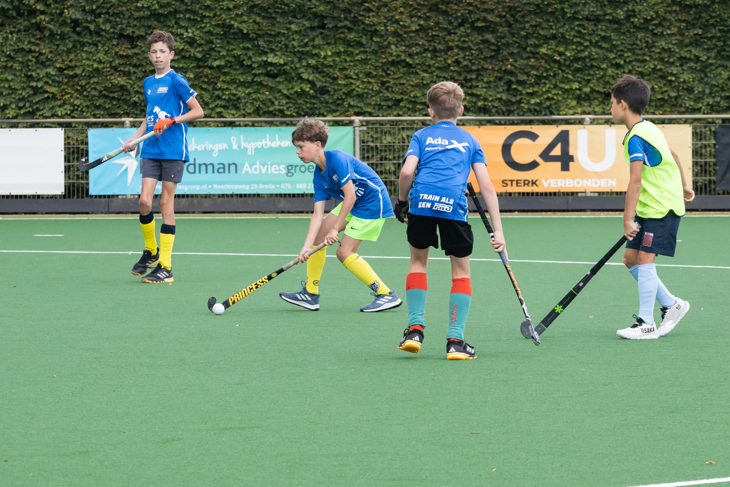 Jonge spelers tijdens een ProHockey zomerkamp bij hockeyclub Prinsenbeek concentreren zich op een wedstrijd op het kunstgrasveld.